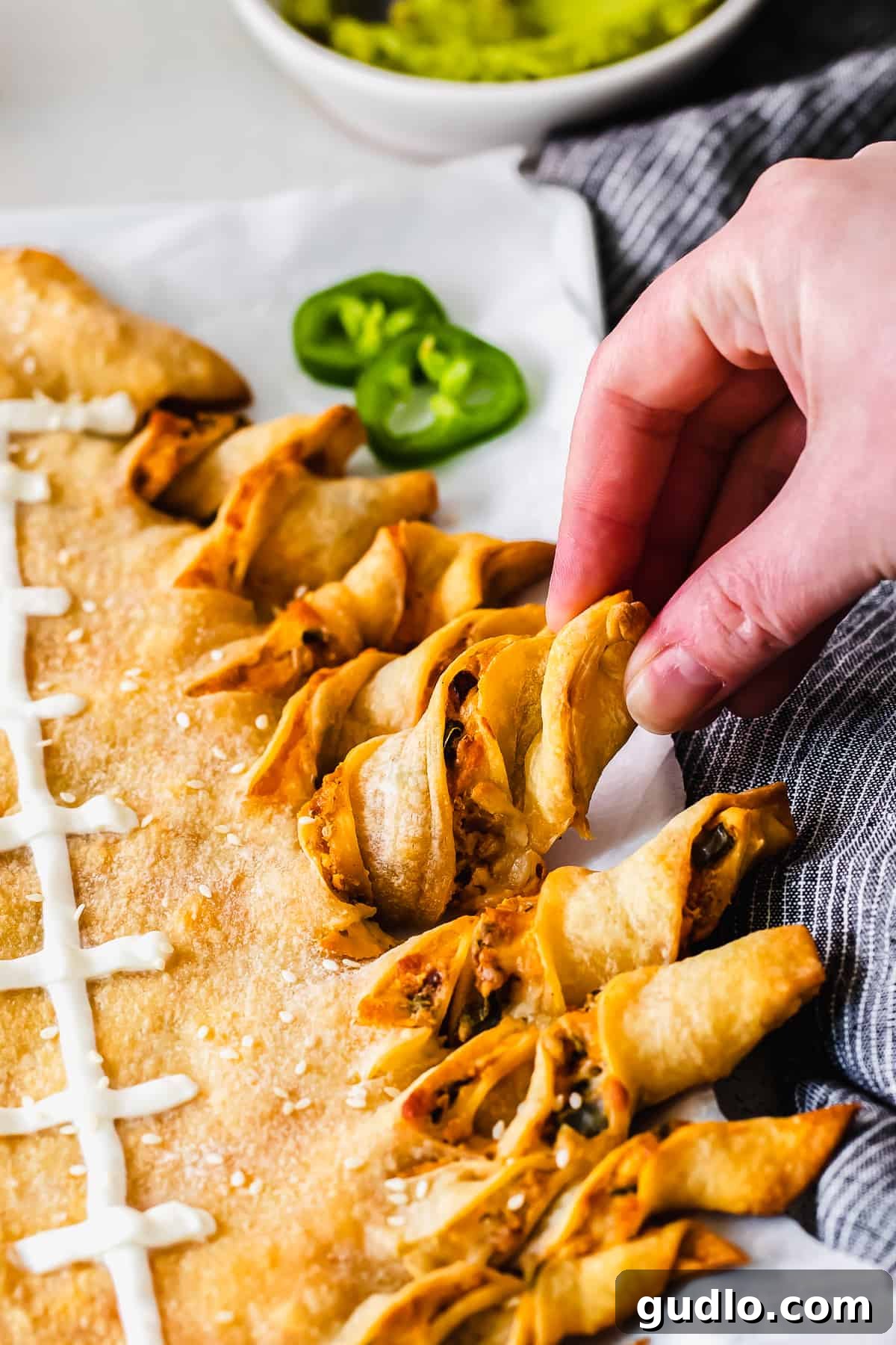 It's game day and we're making these jalapeño popper football-shaped stuffed cheesy breadsticks! This appetizer is a deliciously perfect dish to pass. hand pulling off a cheesy breadstick from the football