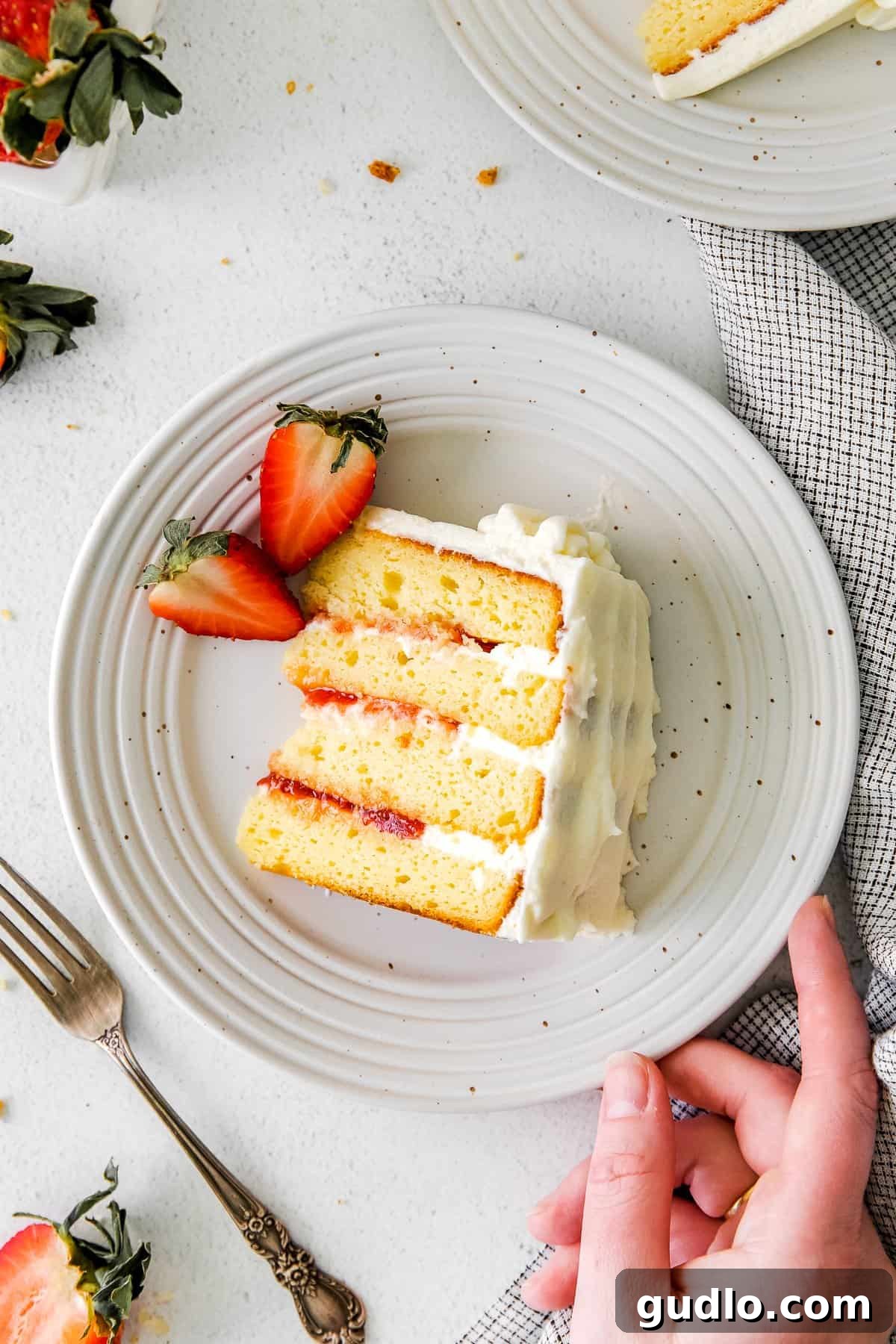 Dreamy Strawberry Ricotta Layer Cake 13 A close-up of a fork taking a bite out of a fluffy slice of strawberry ricotta cake, showing the layers of cake, frosting, and preserves.