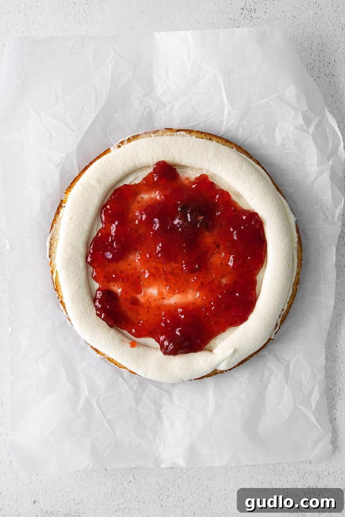 Dreamy Strawberry Ricotta Layer Cake 9 A generous layer of vibrant strawberry preserves spread evenly over a ricotta cake layer, enclosed by a piped frosting dam.