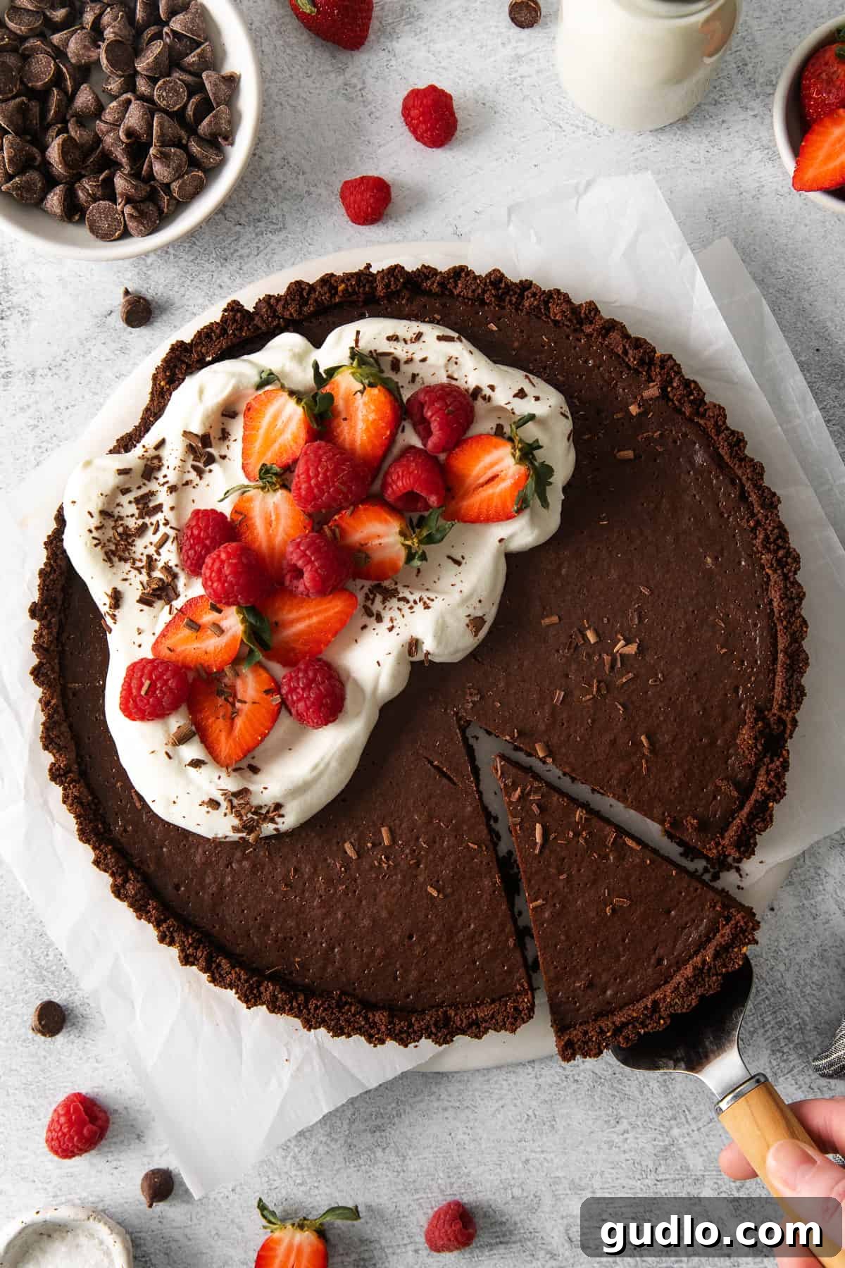 A finished chocolate tart adorned with fresh whipped cream, vibrant strawberries, and ripe raspberries, ready to be served.