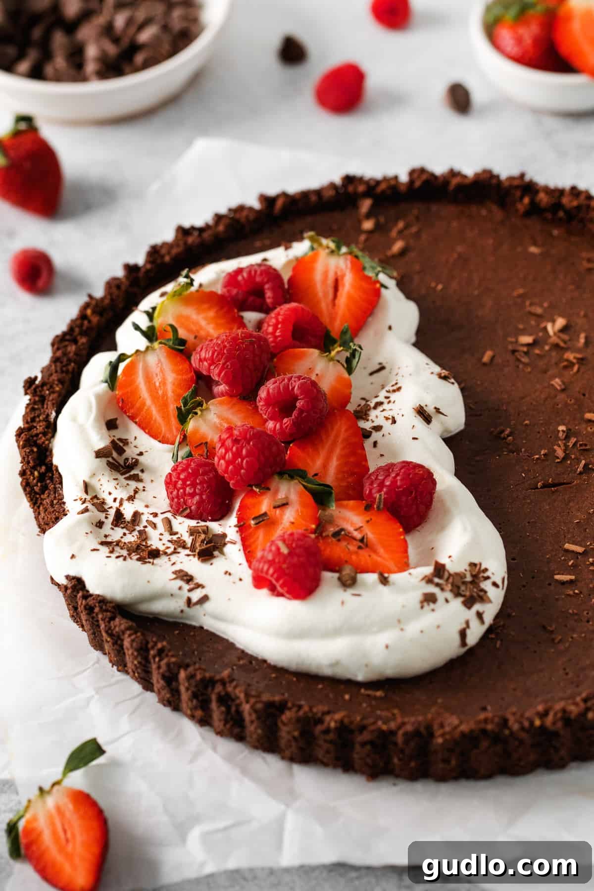 A close-up of a finished chocolate tart with whipped cream and fresh berries, ready to be enjoyed.