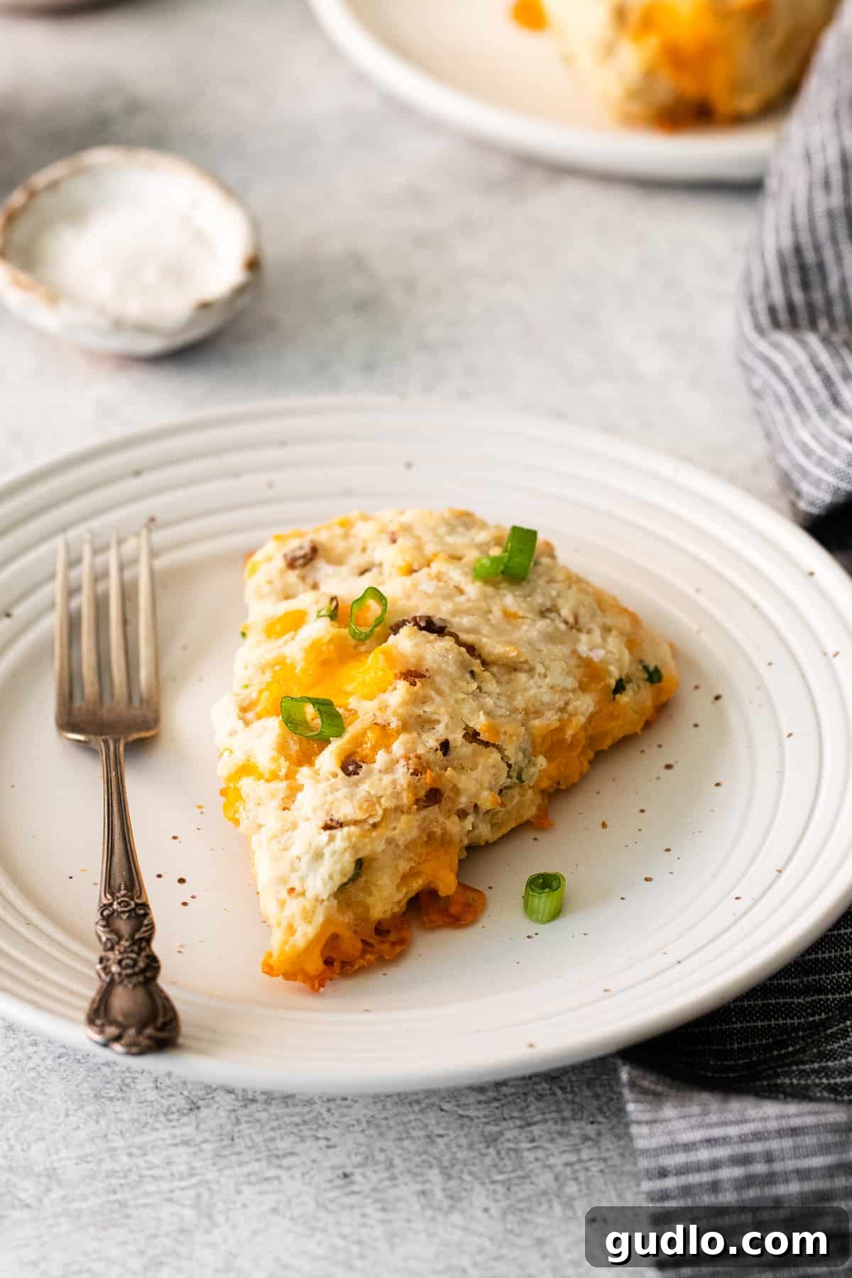 Individual Savory Scone Serving A single Bacon Cheddar Scone, perfectly split in half, revealing its fluffy, layered interior and pockets of melted cheddar, presented invitingly on a white plate.