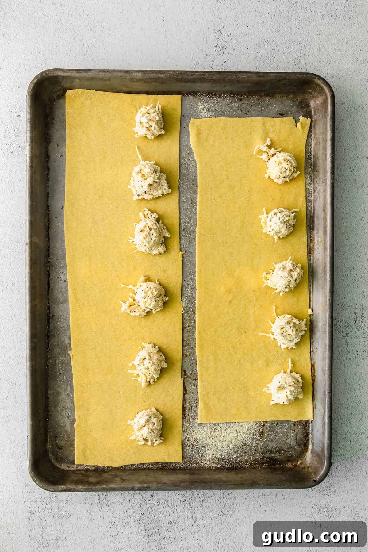 Uncooked ravioli with cheese filling on a baking sheet, ready for sealing.