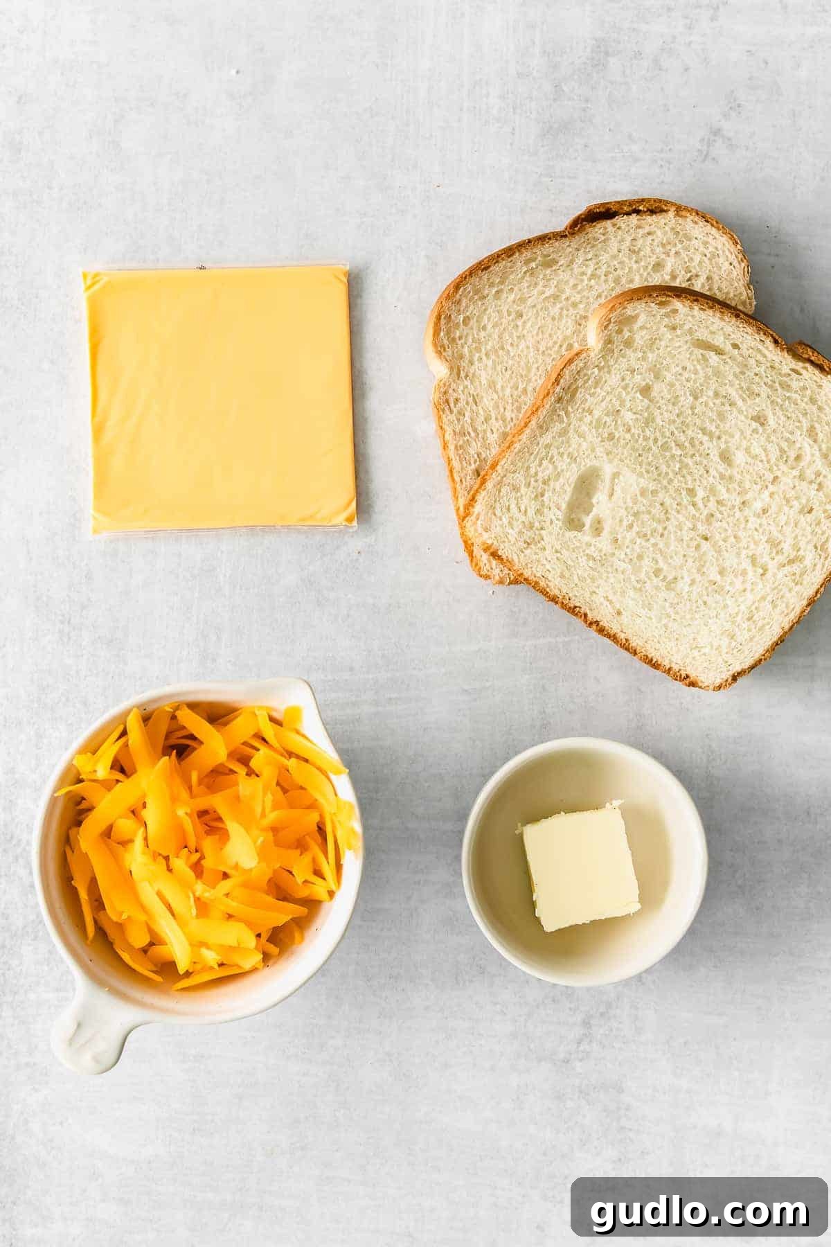 Perfectly crispy on the outside and cheesy on the inside air fryer grilled cheese! Learn how to make grilled cheese in air fryer in less than 15 minutes. Ingredients for air fryer grilled cheese including bread, butter, American cheese, and shredded cheddar on a wooden countertop.