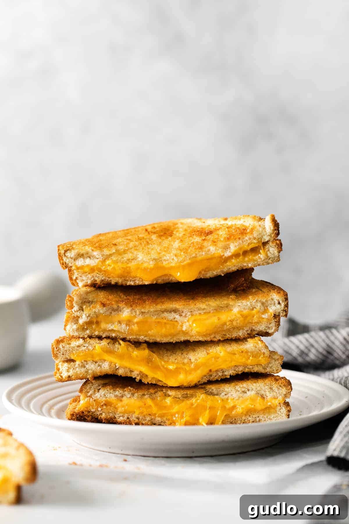 Perfectly crispy on the outside and cheesy on the inside air fryer grilled cheese! Learn how to make grilled cheese in air fryer in less than 15 minutes. A stack of golden-brown air fryer grilled cheese sandwiches on a cutting board, showing their crispy crusts and melted cheese.