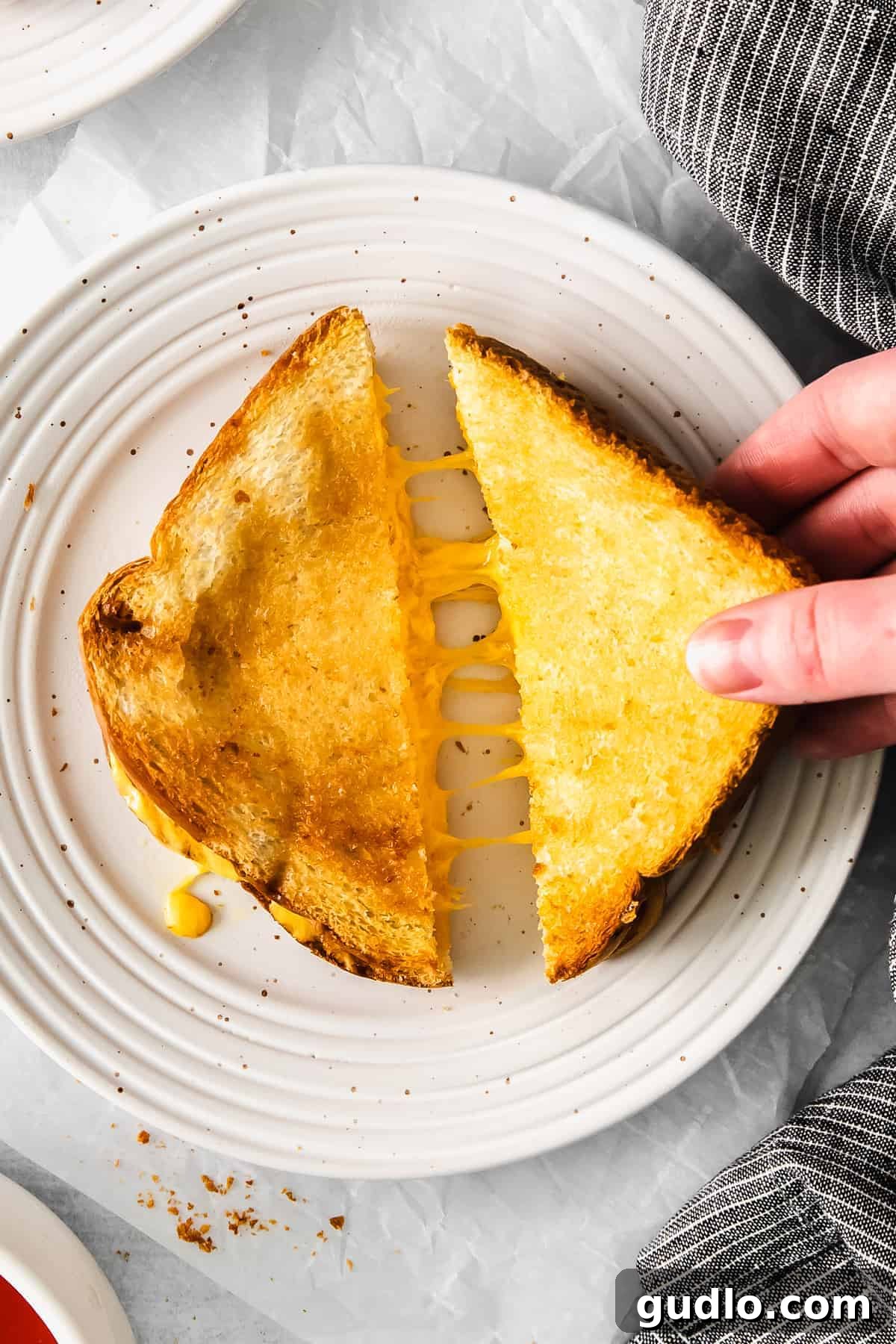 Crispy, perfect air fryer grilled cheese is ready in less than 15 minutes and only requires 4 ingredients! A single air fryer grilled cheese sandwich cut in half on a white plate, revealing the melted, gooey cheese inside.