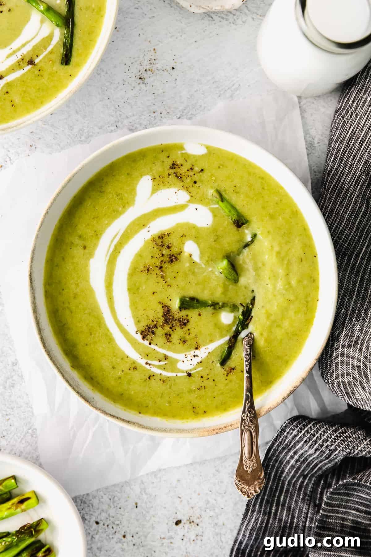 A bowl of creamy roasted asparagus soup, garnished with fresh herbs and a drizzle of cream.