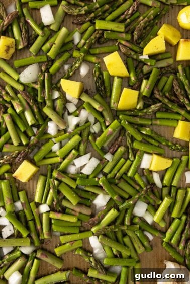 Roasted vegetables including asparagus, onion, potato, and garlic on a baking sheet.