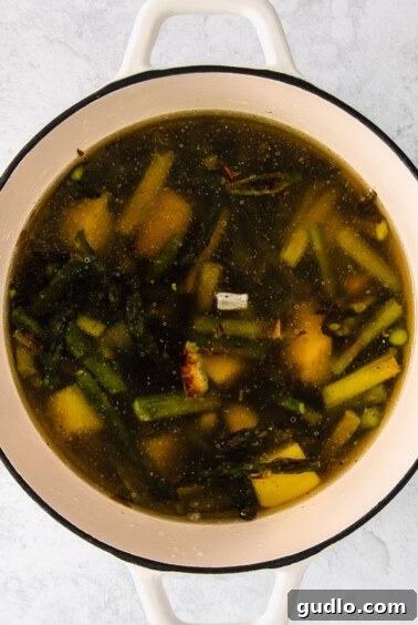 Roasted vegetables simmering in broth in a large pot.
