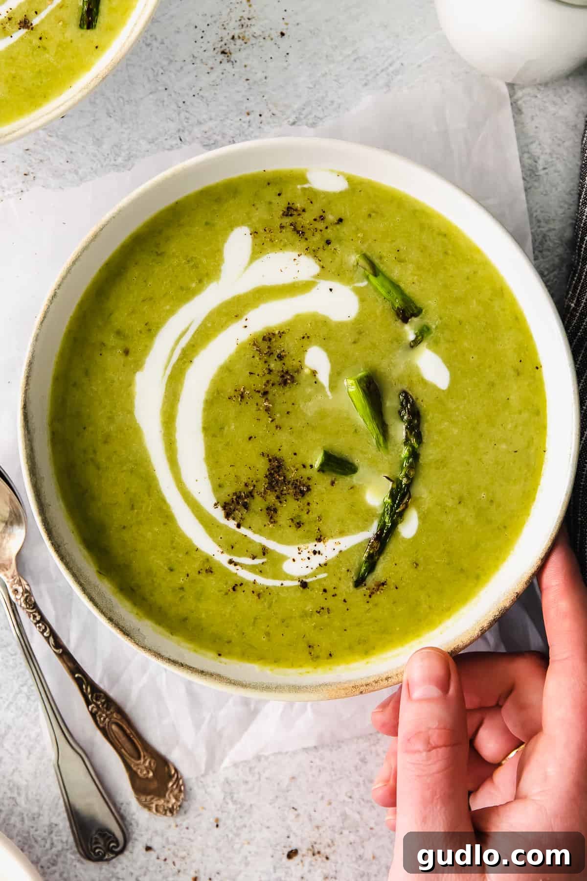 A beautifully presented bowl of creamy roasted asparagus soup, garnished with a sprig of fresh herb.