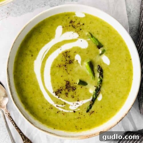 A bowl of creamy asparagus soup garnished with fresh herbs.