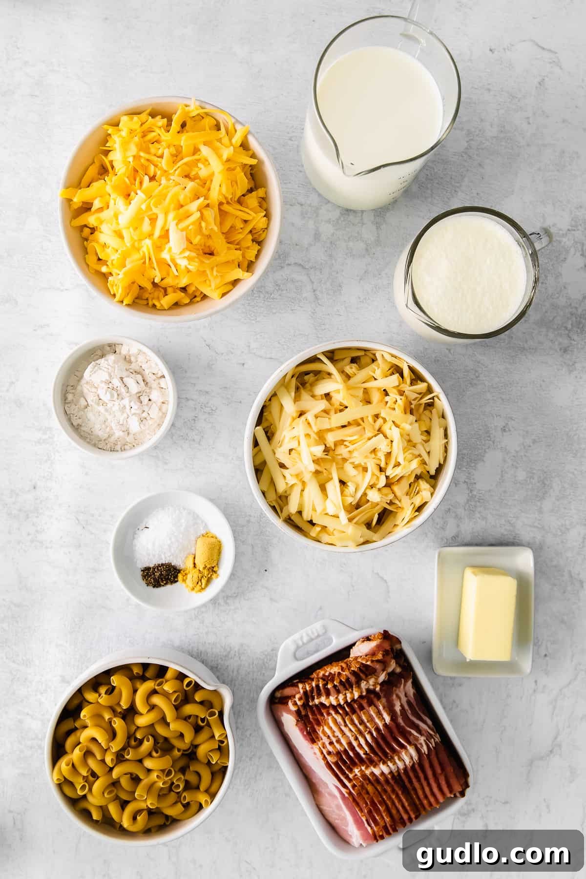 Neatly arranged ingredients for bacon mac and cheese in small, pristine white dishes.