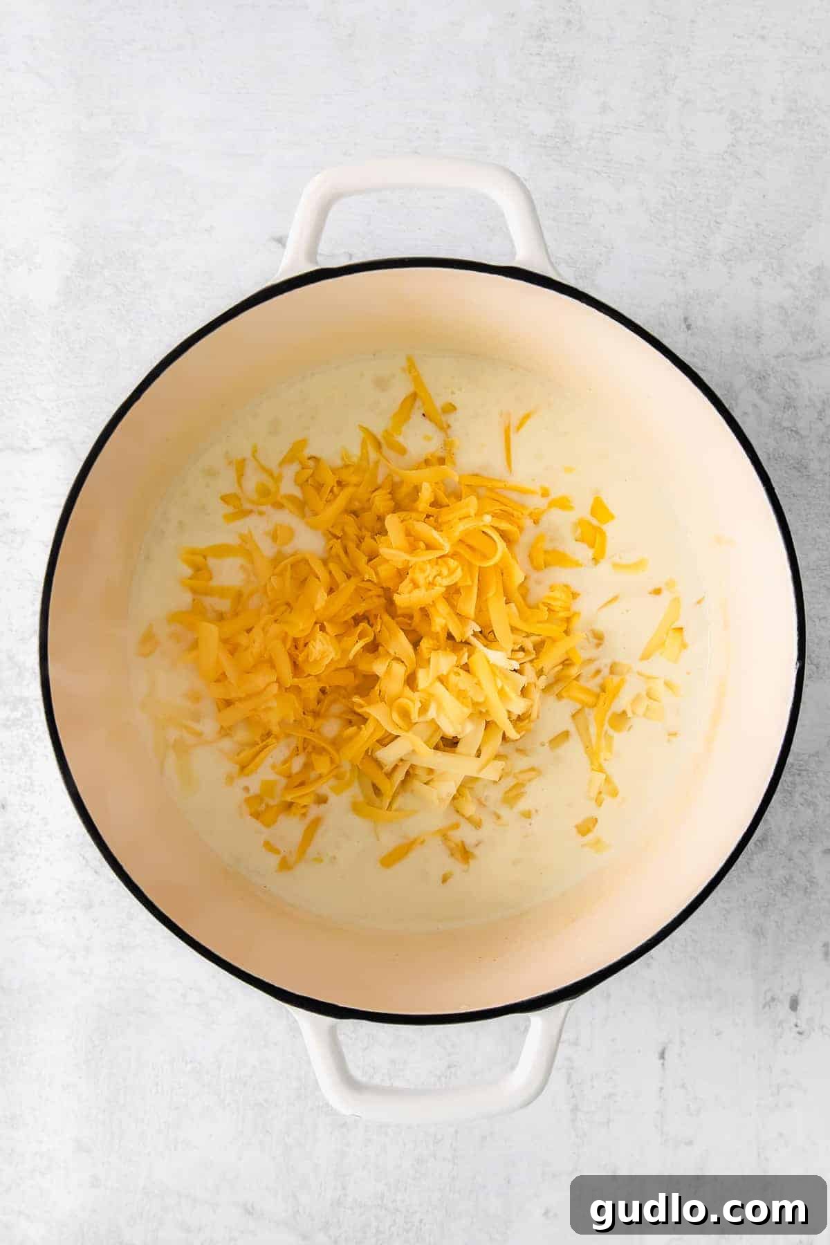 A creamy, golden cheese roux simmering in a pot, with shredded cheddar cheese about to be incorporated.