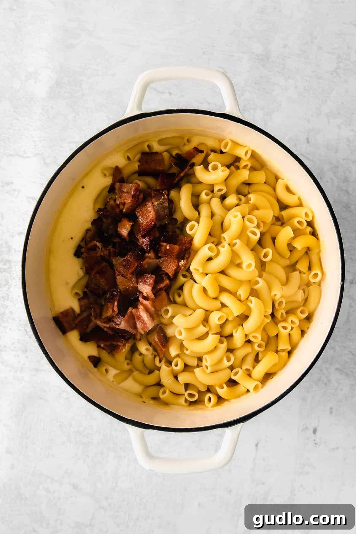 A Dutch oven brimming with perfectly cooked macaroni noodles, crispy bacon pieces, and a rich, creamy cheese sauce, all ready for the oven.