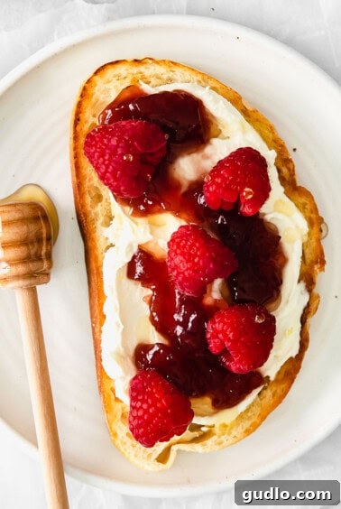 A sweet mascarpone toast adorned with jam and fresh raspberries, drizzled with honey.