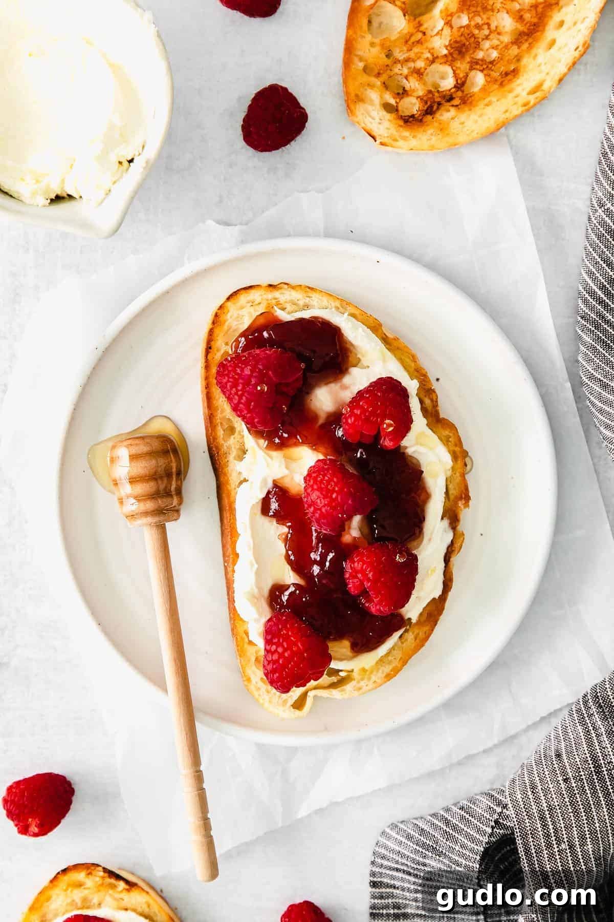 A vibrant slice of mascarpone toast topped with fresh raspberries and a generous spread of glistening raspberry preserves, offering a delightful sweet treat.