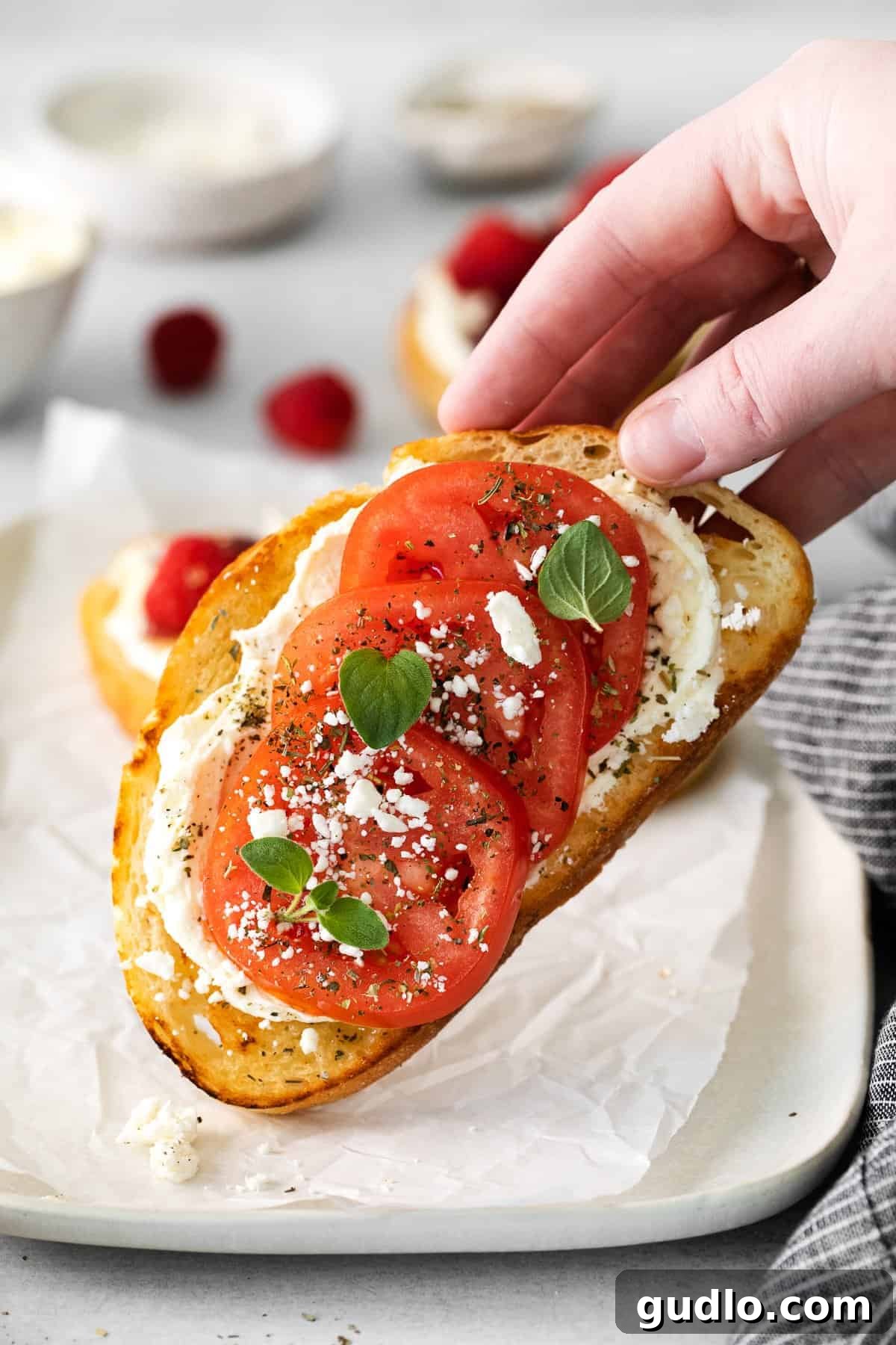 A savory slice of mascarpone toast adorned with marinated cherry tomatoes, crumbled feta cheese, and fresh basil leaves, showcasing a Mediterranean flavor profile.