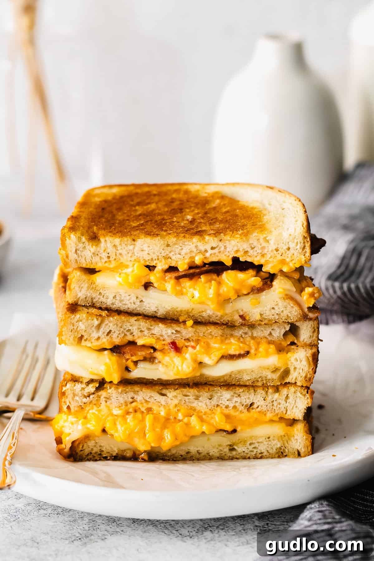 A beautifully stacked grilled cheese sandwich, golden brown and oozing with cheese and bacon, ready to be enjoyed.
