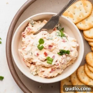 A bowl of creamy pimento cheese dip, garnished with fresh herbs, served alongside crispy crackers.