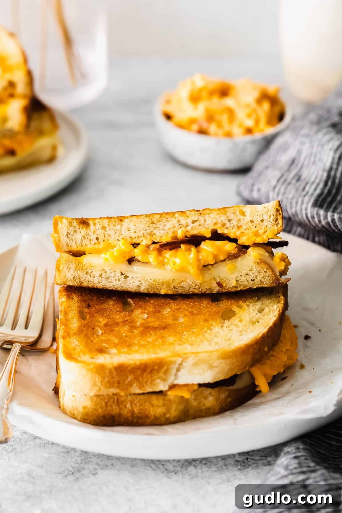 Two fancy grilled cheese sandwiches, perfectly stacked and golden, revealing the melted cheese and bacon inside.