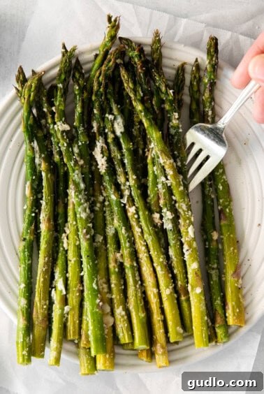Parmesan-Crusted Asparagus 6 A serving of roasted parmesan asparagus on a plate, with a fork, ready to eat.