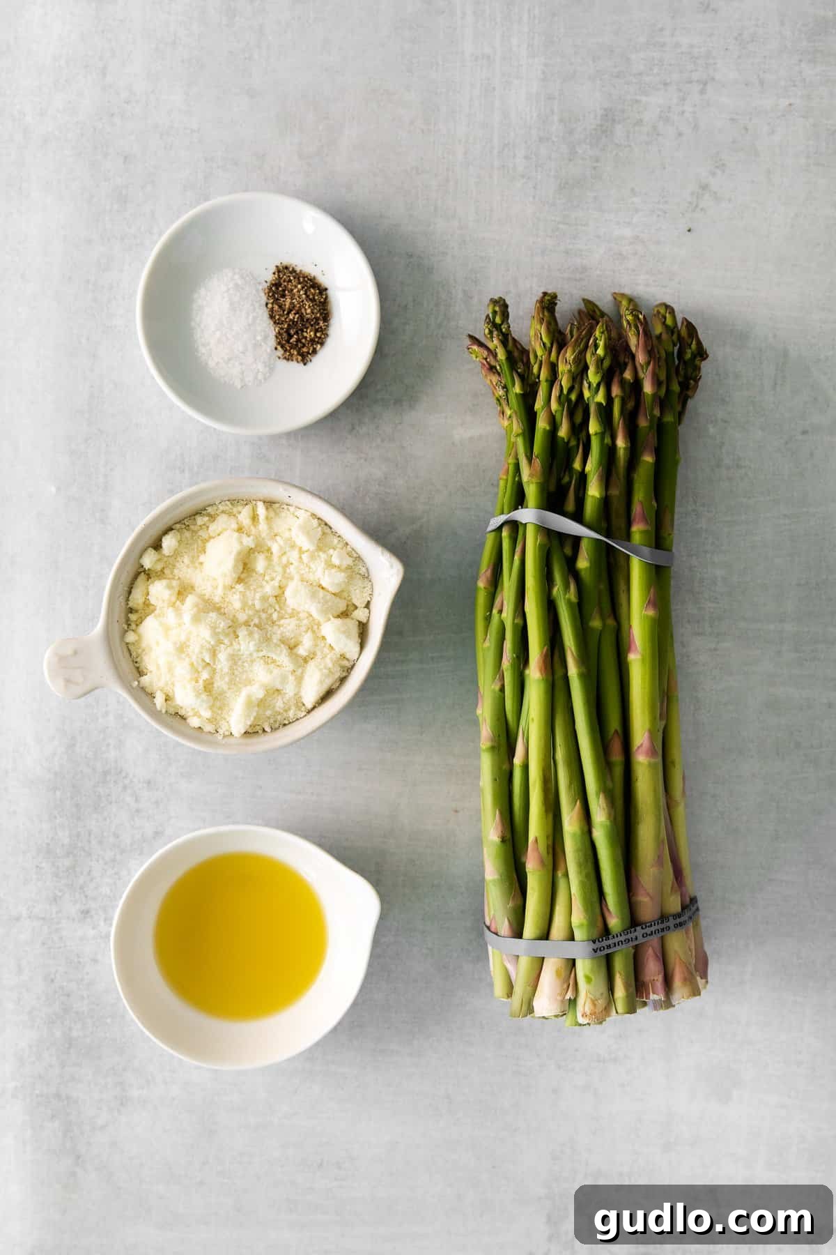 Essential Ingredients for Perfect Roasted Parmesan Asparagus Fresh asparagus spears, olive oil, salt, pepper, and a bowl of grated parmesan cheese, laid out as ingredients for the recipe.