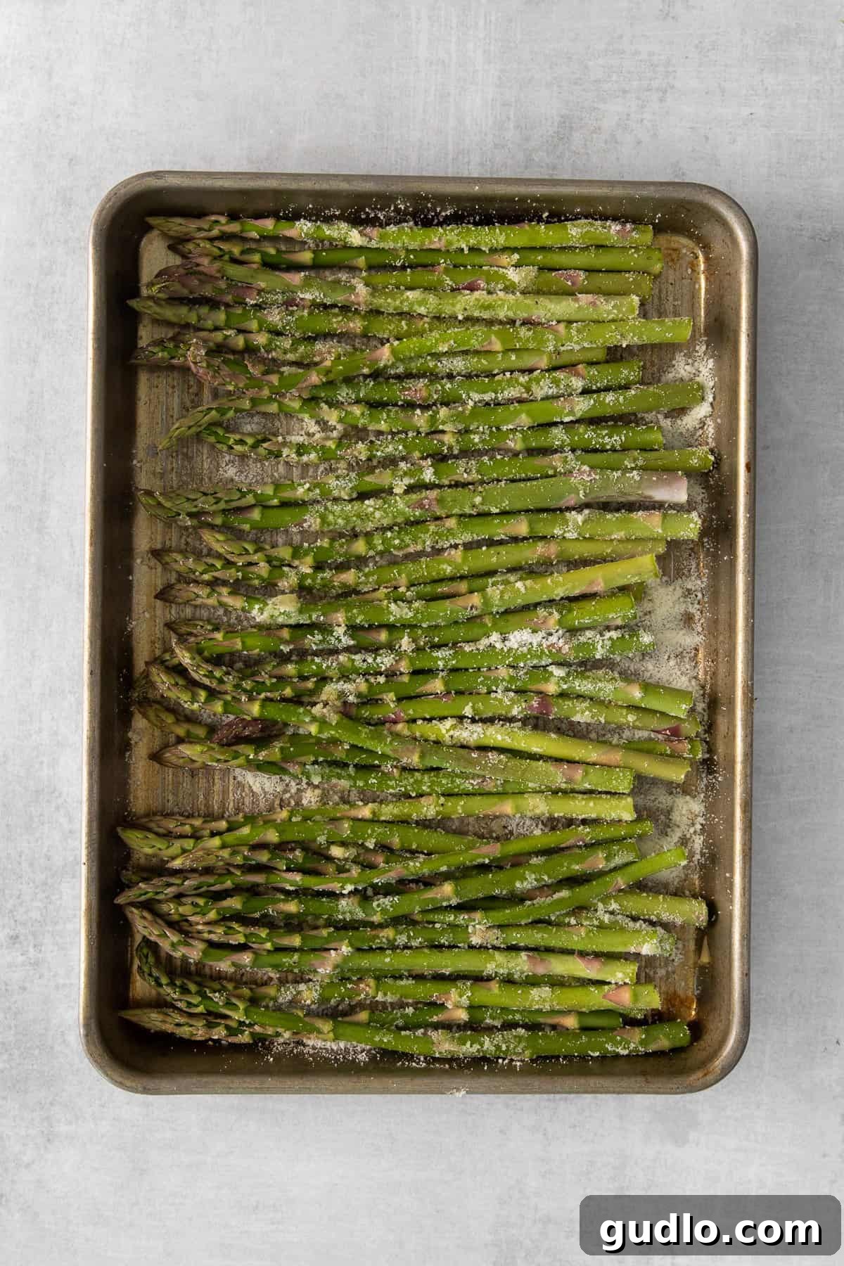 Preparing Parmesan Asparagus for Roasting Parmesan asparagus spears spread out on a baking sheet, glistening with olive oil and seasoning, ready for roasting.