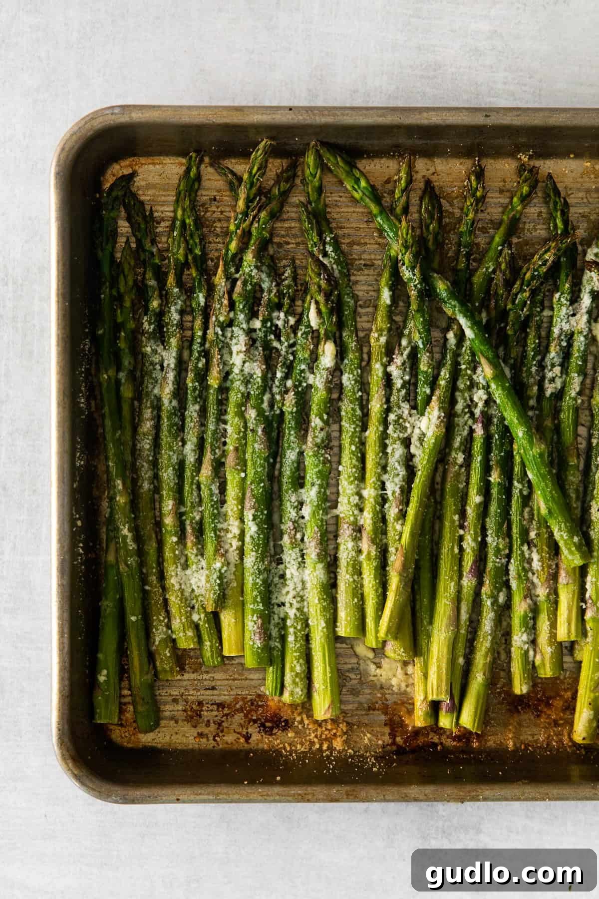 Roasted Parmesan Asparagus: Perfectly Cooked and Ready to Serve Freshly roasted parmesan asparagus spears scattered on a baking sheet, with some cheese slightly browned and crispy.