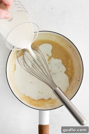 Creamy Garlic Parmesan Sauce 11 Milk being slowly poured into a saucepan with a roux, while being continuously whisked to create a smooth sauce.