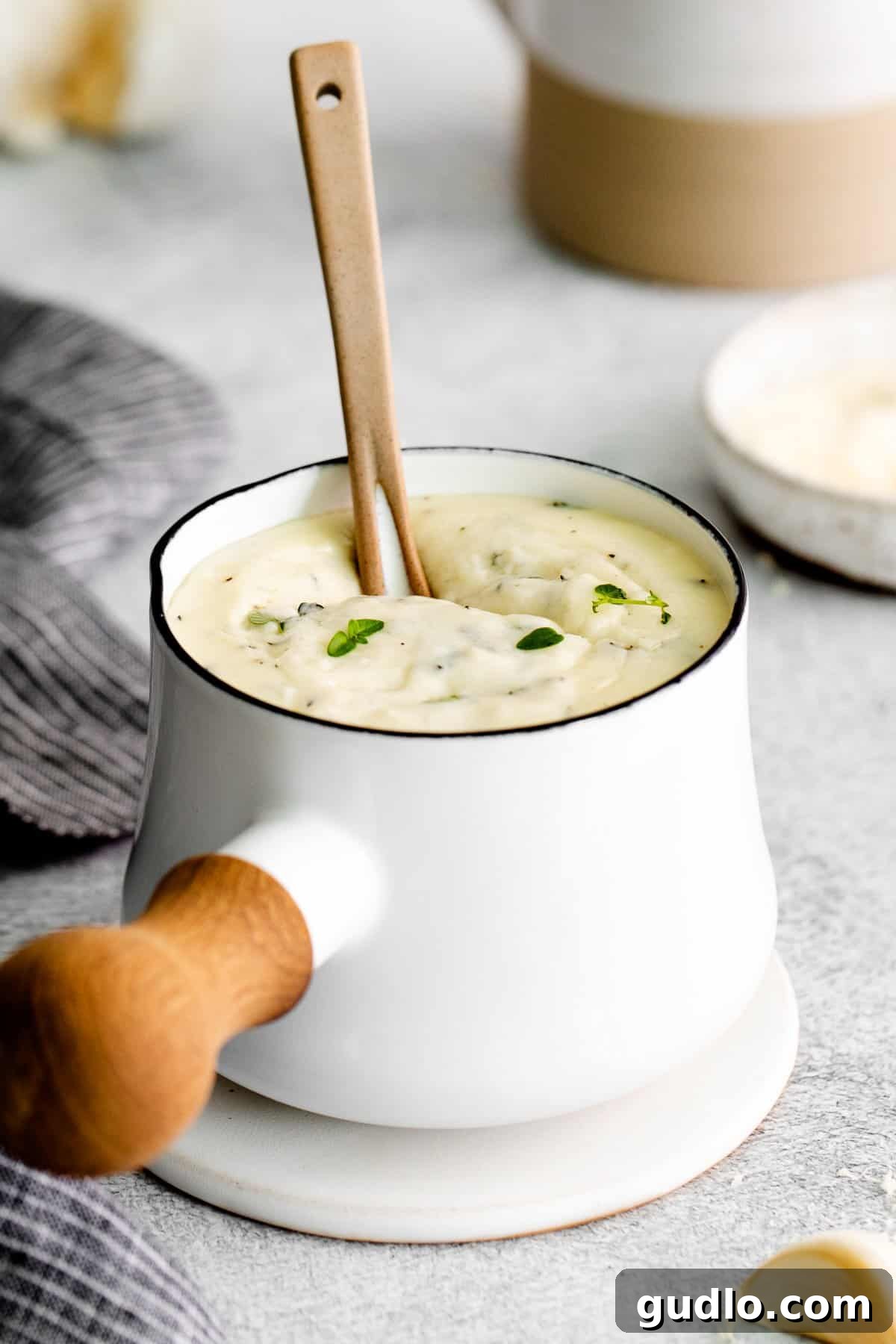 Creamy Garlic Parmesan Sauce 6 A small, elegant pot filled with perfectly made garlic parmesan sauce, garnished with fresh herbs, ready to be served.