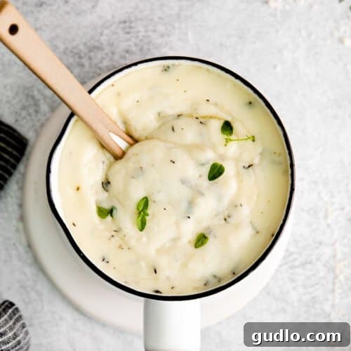 Parmesan garlic sauce in a small pot, garnished with fresh herbs, showcasing its rich texture.
