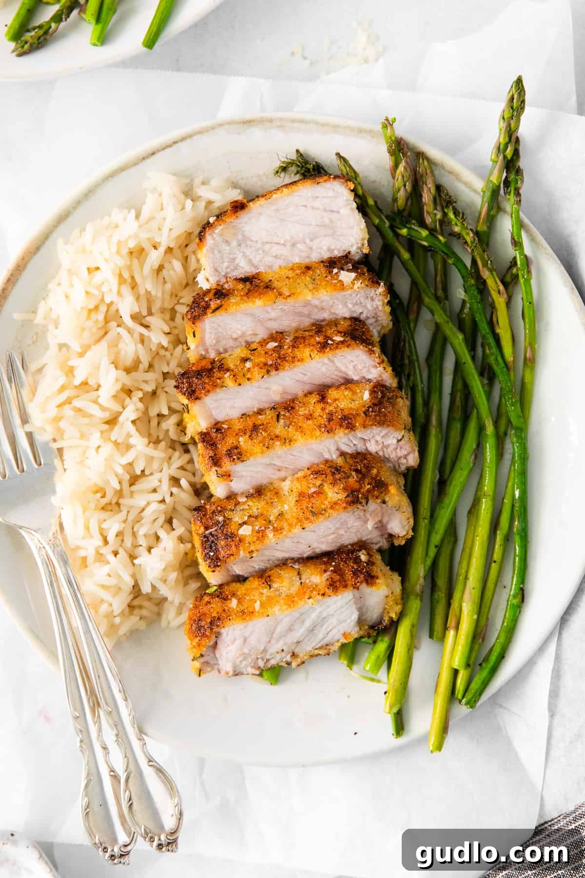 Golden Parmesan Pork Chops 9 A plate featuring parmesan crusted pork chops, green asparagus, and rice, ready to be served.