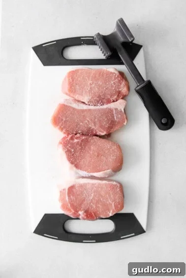 Golden Parmesan Pork Chops 11 Pork chops being pounded on a cutting board.