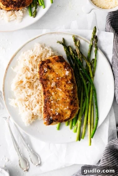 Golden Parmesan Pork Chops 14 Cooked pork chop on a plate with asparagus and rice.