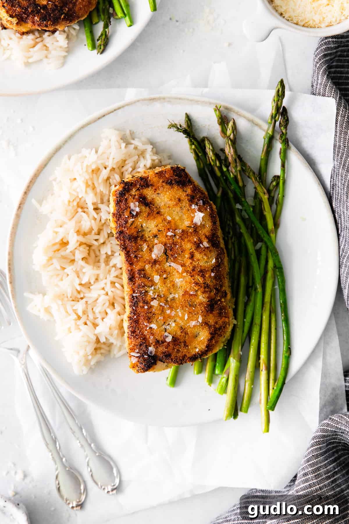Golden Parmesan Pork Chops 8 A cooked parmesan crusted pork chop on a plate with asparagus and rice.
