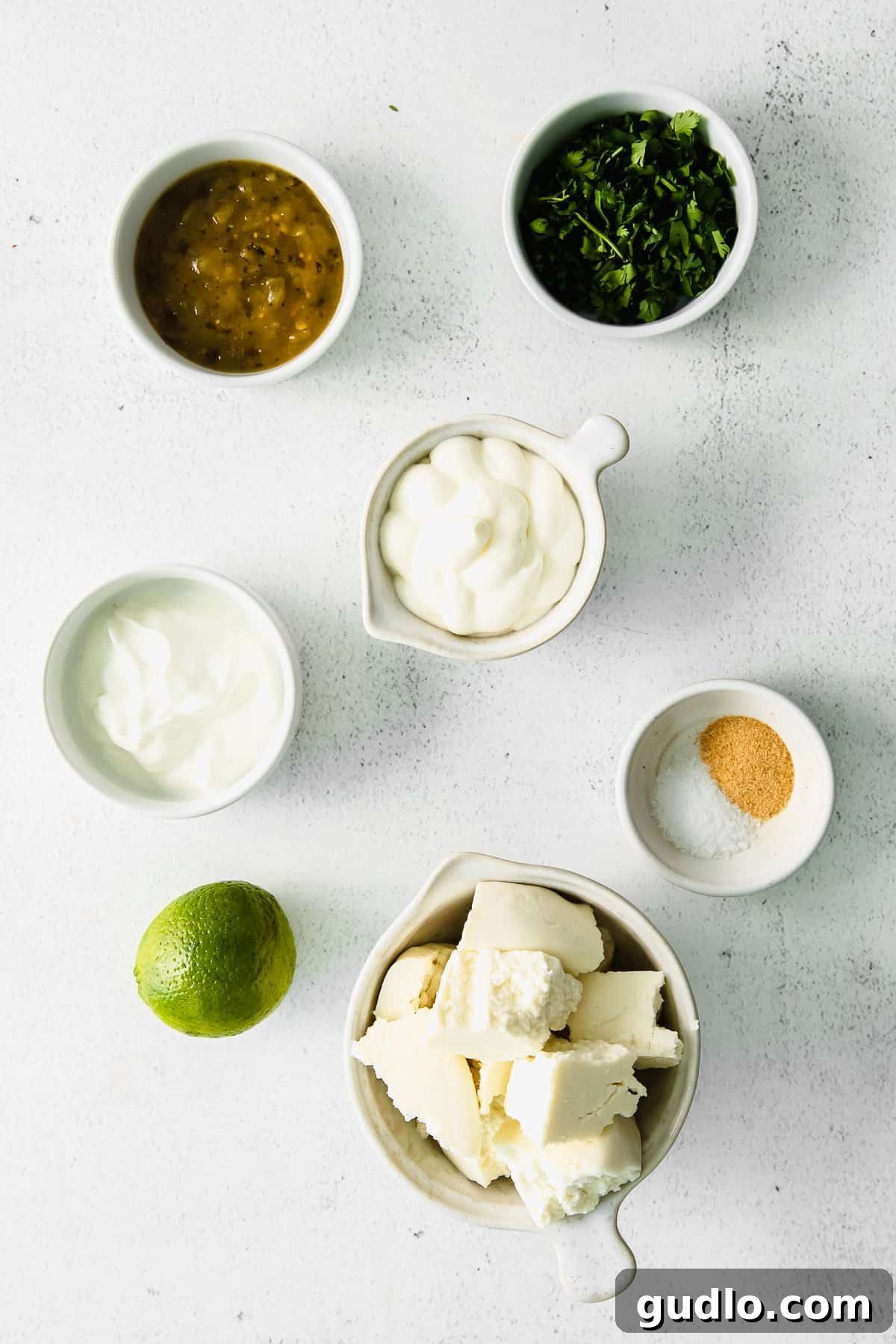 Use this simple recipe for queso fresco cheese dip for chips, raw veggies, or as a topping for enchiladas or quesadillas! Fresh ingredients laid out on a kitchen countertop, including queso fresco, limes, cilantro, and yogurt, ready for making the dip.