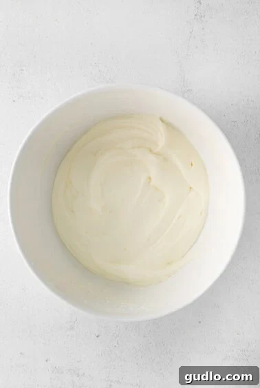 Cream cheese frosting in a bowl, being whipped by an electric mixer.