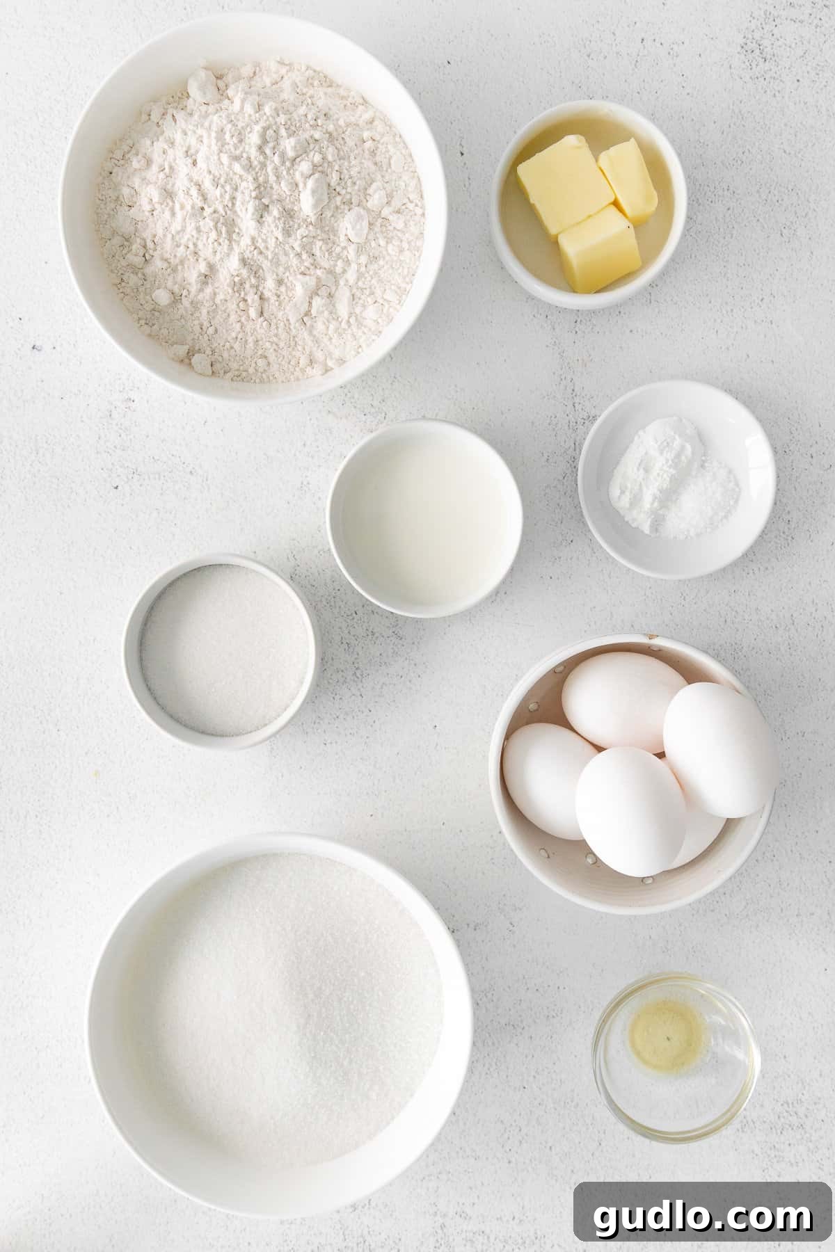 Assortment of Tres Leches cake ingredients laid out on a clean kitchen countertop, including milk cans, eggs, butter, flour, and vanilla.