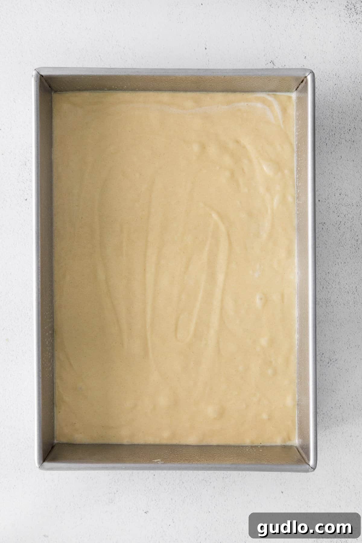 Vanilla cake batter poured evenly into a 9x13 inch baking pan, ready for the oven.