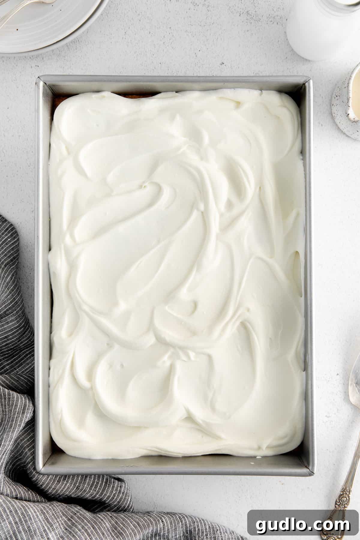 Frosted Tres Leches cake in a baking pan, covered and ready to chill in the refrigerator.