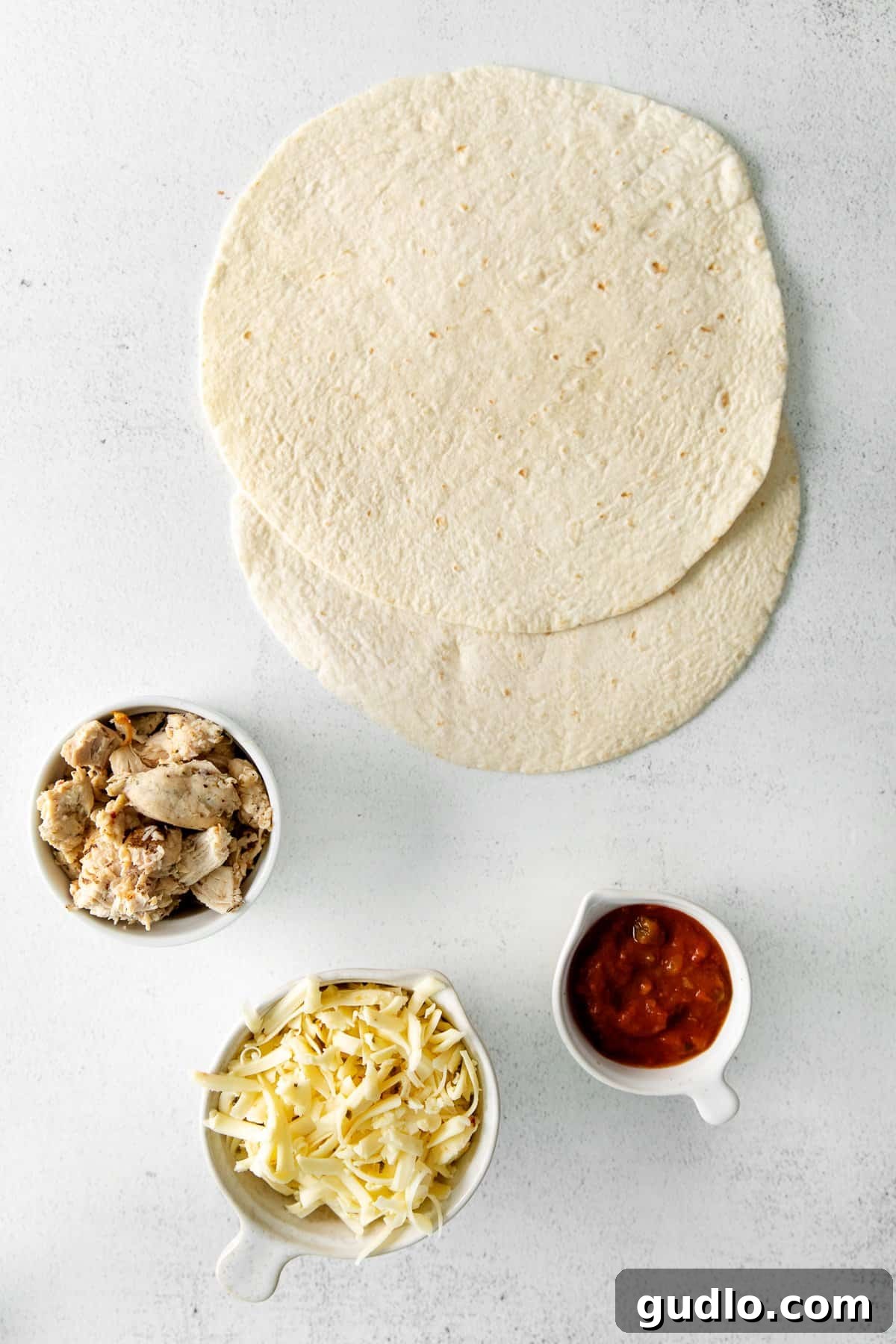 Essential Air Fryer Quesadilla Ingredients The four simple ingredients for air fryer quesadillas laid out on a kitchen countertop: shredded chicken, salsa, shredded cheese, and flour tortillas.