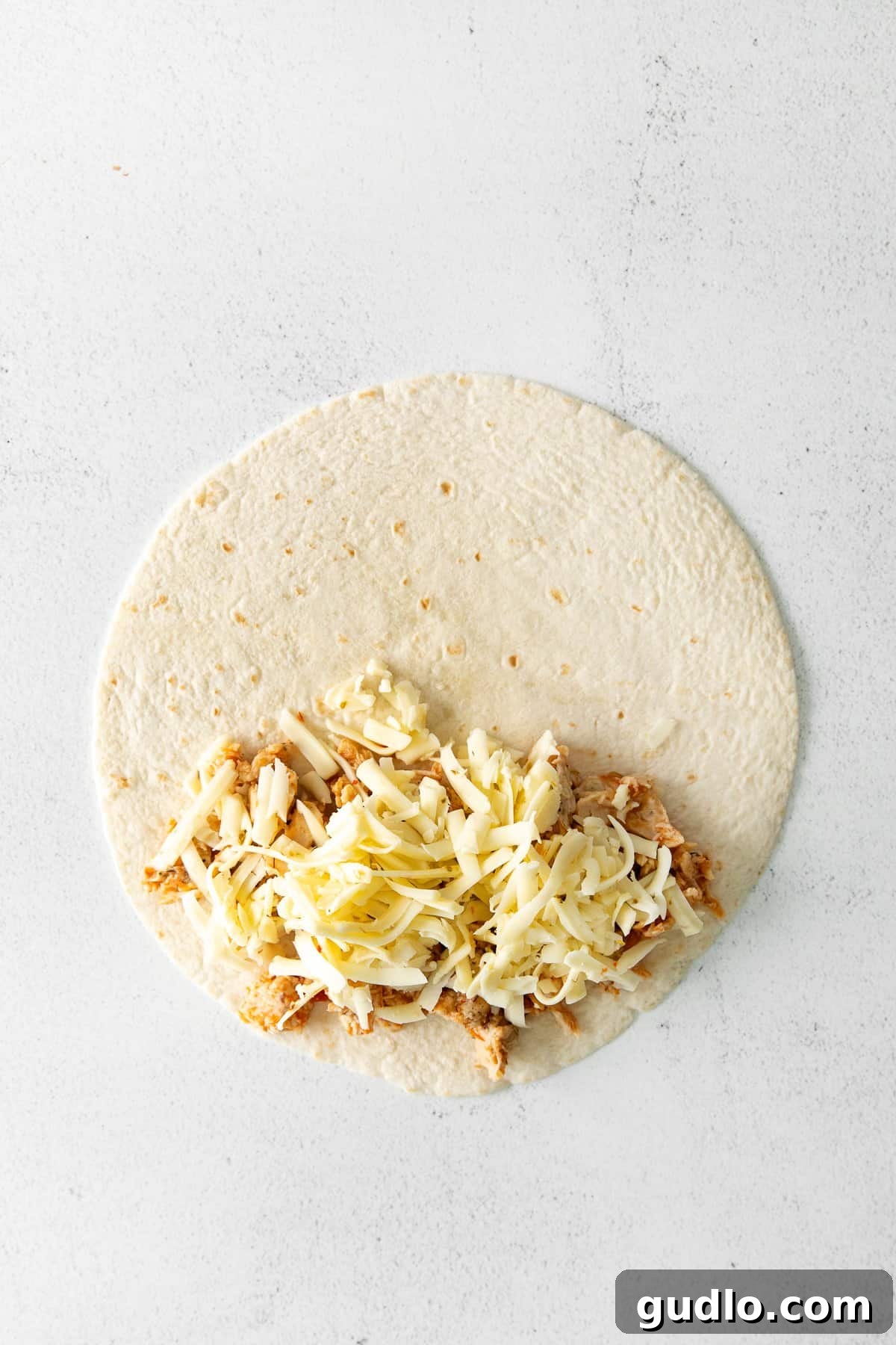 Assembling the Air Fryer Quesadilla A flour tortilla with shredded chicken and cheese filling on one half, folded over and secured with toothpicks, ready for air frying.