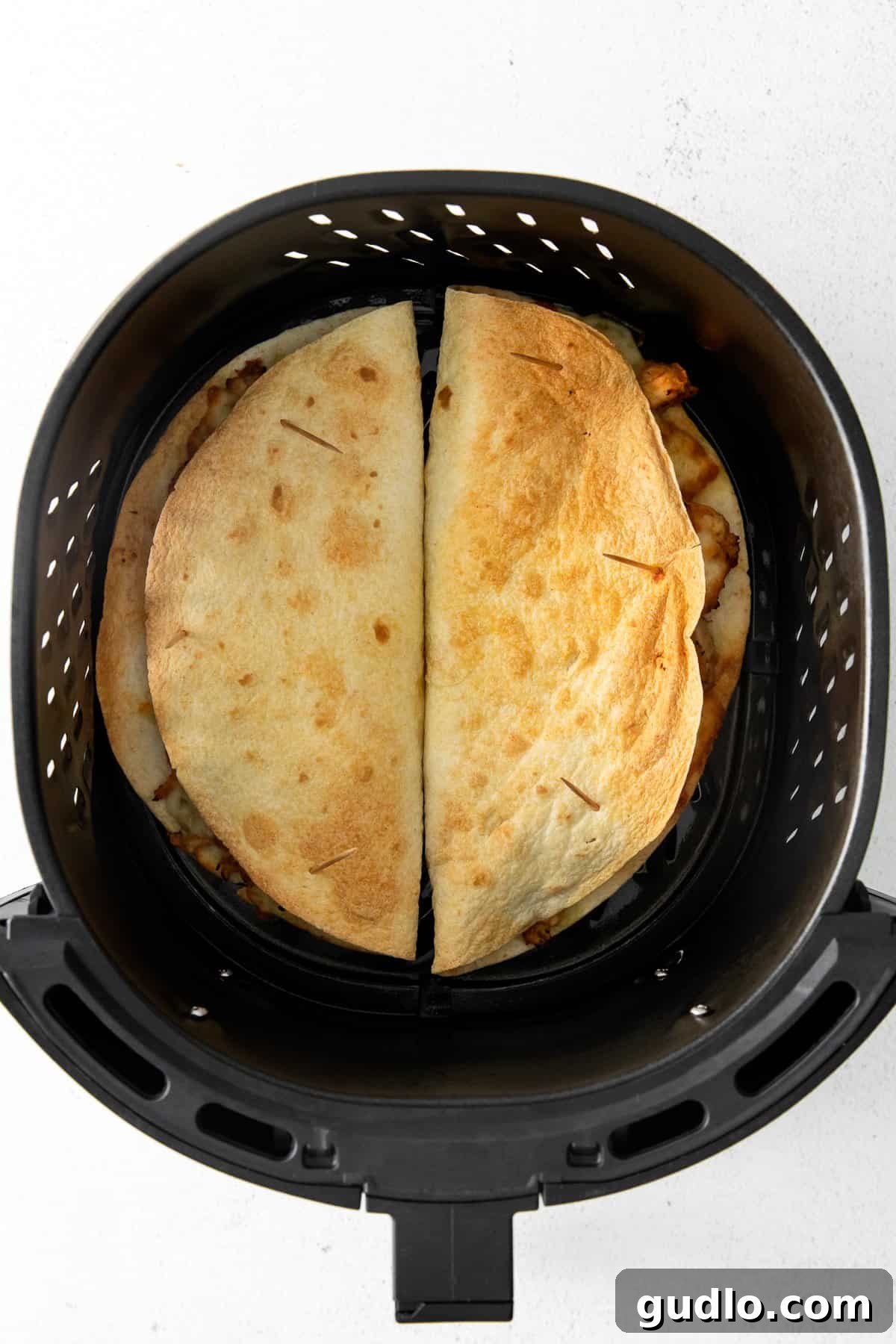 Air Frying Quesadillas for Crispiness Two chicken and cheese quesadillas cooking in an air fryer basket, showing their golden-brown and crispy exterior.