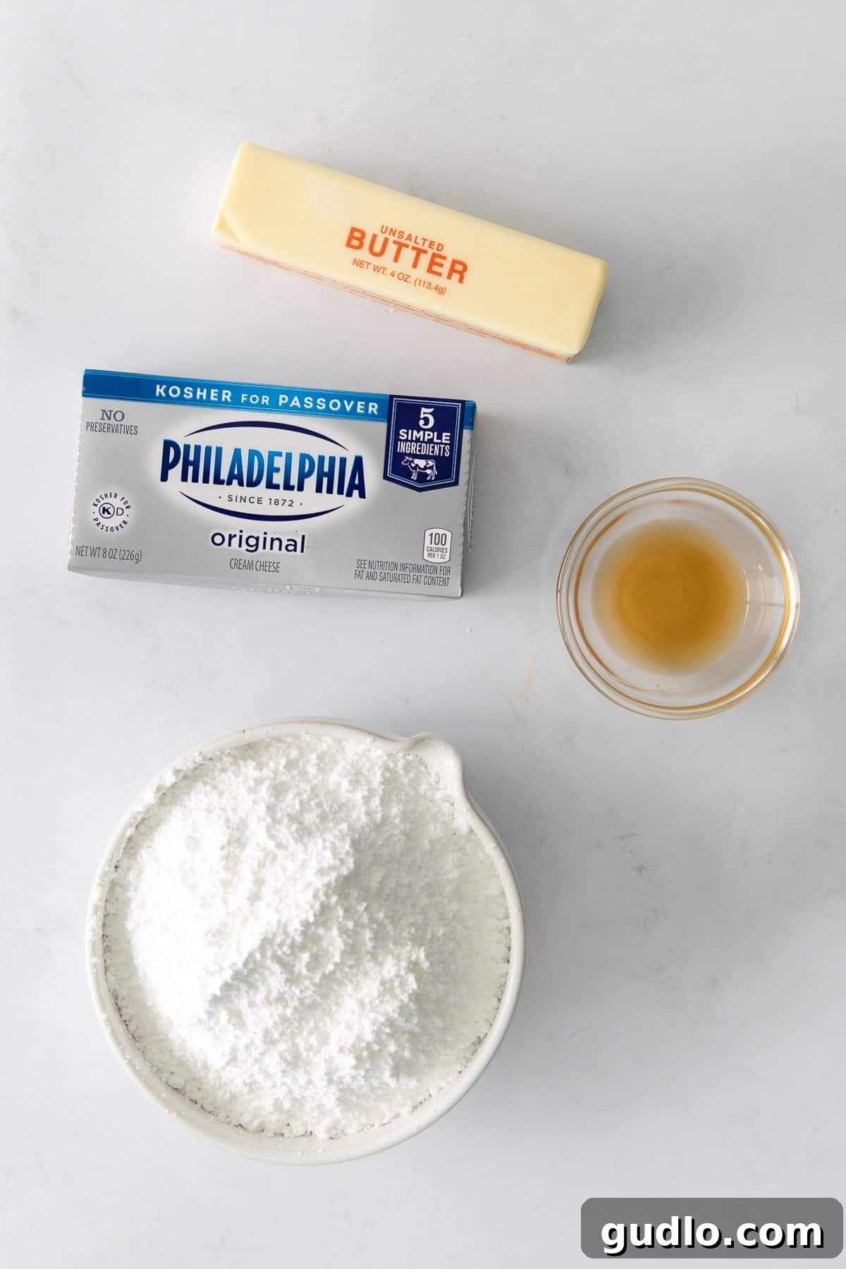 Velvety Vanilla Cream Cheese Frosting 3 The four essential ingredients for cream cheese frosting neatly arranged on a countertop: butter, cream cheese, powdered sugar, and vanilla extract.