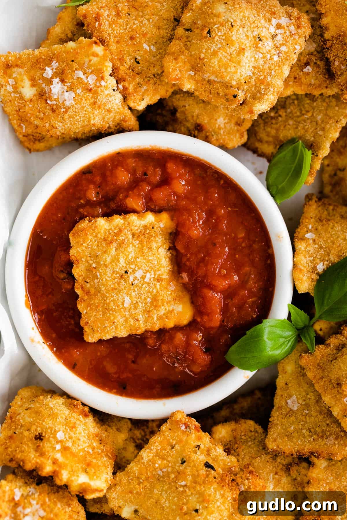 A single, perfectly air-fried ravioli, golden and crispy, rests in a small pool of vibrant red marinara sauce, showcasing its delicious breaded exterior.