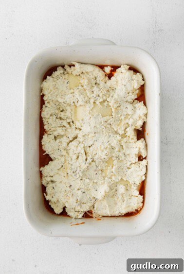 Ricotta mixture spread over ravioli in a baking dish.