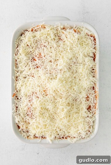 Layer of shredded mozzarella cheese over sauce in a casserole dish.