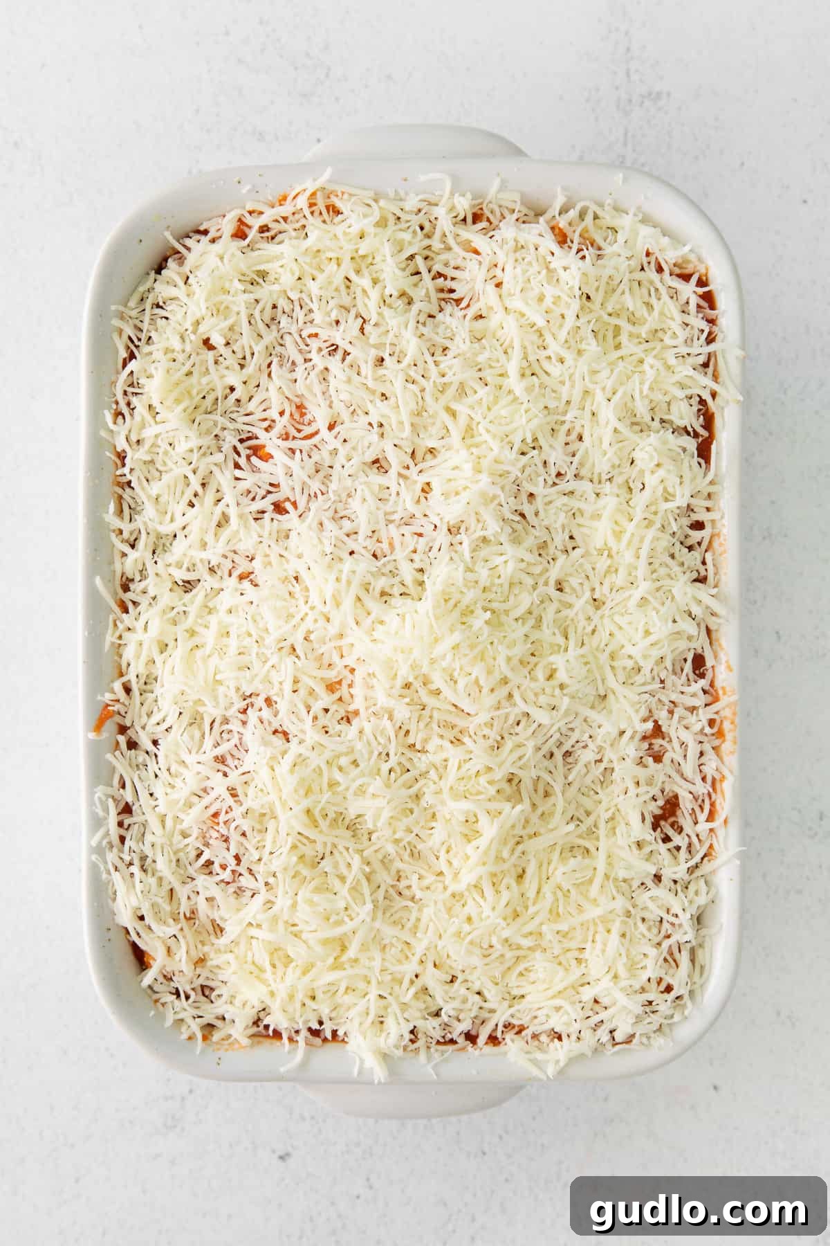 Ravioli lasagna generously covered in a thick, golden layer of shredded mozzarella cheese, ready for baking.
