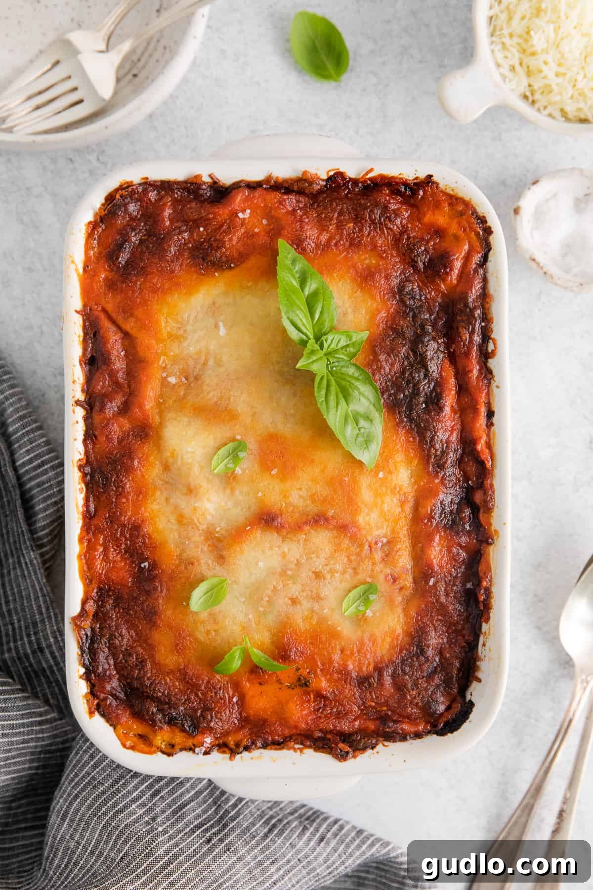 Freshly baked ravioli lasagna in a white casserole dish, garnished with vibrant green basil leaves.