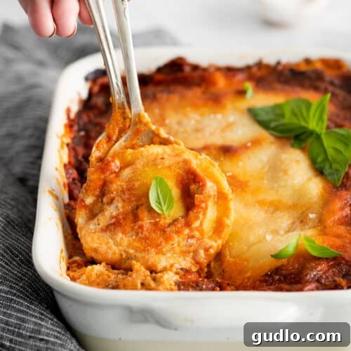 Lasagna in a white baking dish with a serving fork, ready to be dished out.